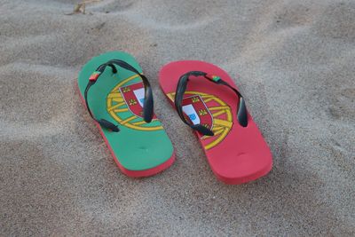 High angle view of portuguese flag on flip-flops at sandy beach