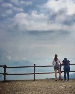 Rear view of friends standing by railing against sea