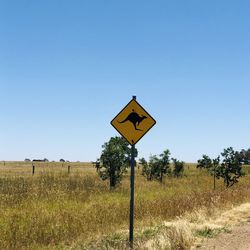 Road sign on field against clear sky