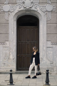 Full length of woman standing against door of building