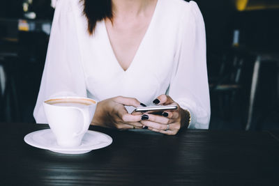 Close-up of woman holding coffee cup on table