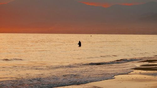 Silhouette people on beach against sky during sunset
