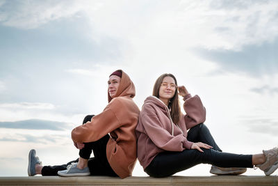 Women sitting on friends against cloudy sky