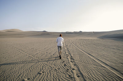 Rear view of man walking on sand at desert