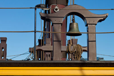 Low angle view of bell on ship against clear blue sky