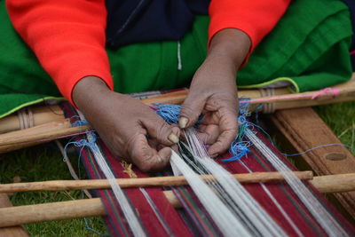 Cropped hands of manual worker weaving textile in workshop