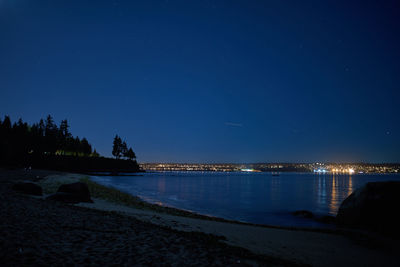 Illuminated city by sea against clear blue sky at night
