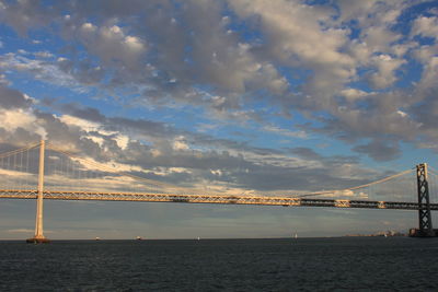 Suspension bridge over sea against cloudy sky