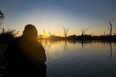 Rear view of silhouette man by lake against sky during sunset