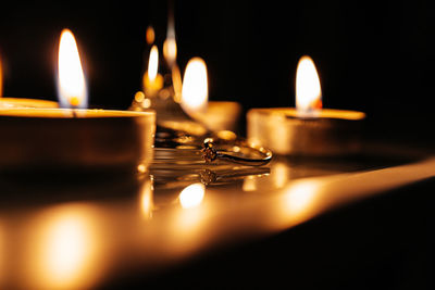 An engagement ring placed on the table between burning candles and a glass of champagne