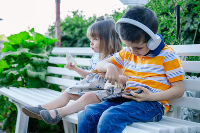 Cute boy listening music with sister on bench