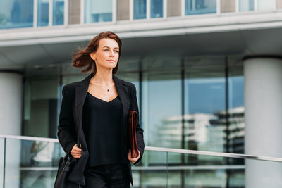 Portrait of young woman standing against building