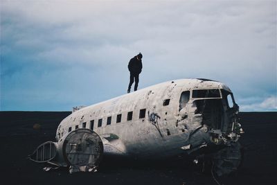 Man standing on solheimasandur plane wreck at black sand beach against sky