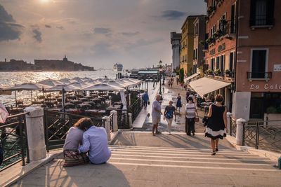 People walking by buildings in city during sunset