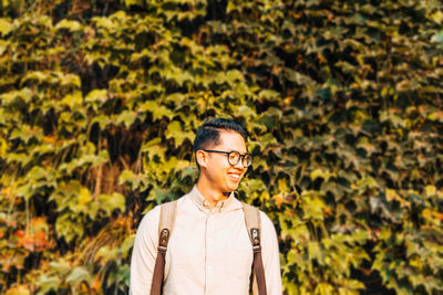 Smiling young man looking away against plants