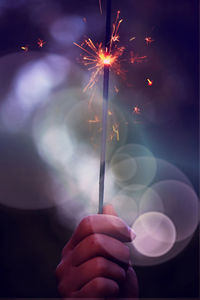 Close-up of cropped hand holding illuminated sparkler at night