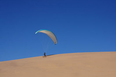 Man paragliding on desert against clear blue sky