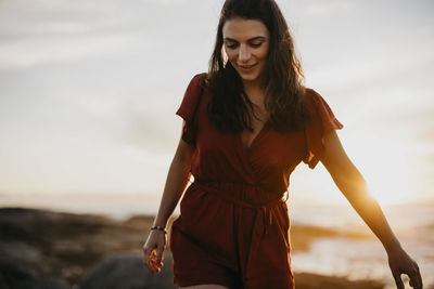 Young woman walking in front of sky at sunset