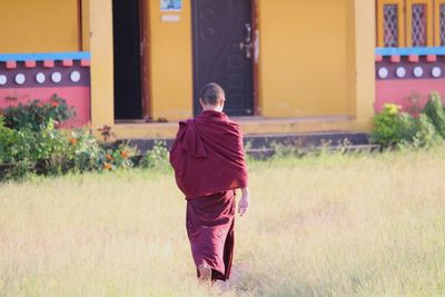 Rear view of buddhist monk walking on field