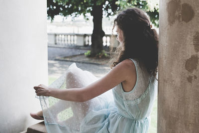 Young curly hair woman in a light blue dress sitting in a pavilion in a garden. side view. summer