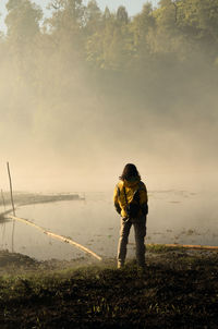 Rear view of man standing by lake against sky