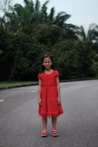 Portrait of cute girl wearing red dress while standing on road