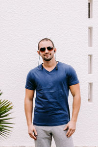 Portrait of young man wearing sunglasses standing against wall