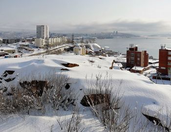 Snow covered buildings in city against sky