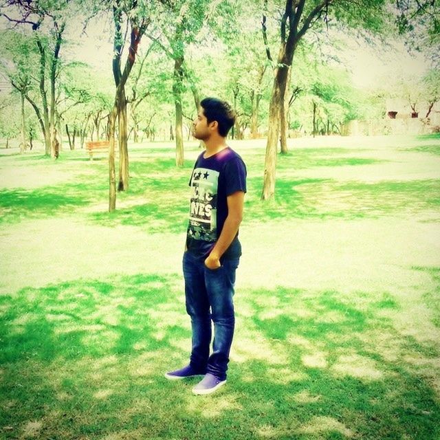 tree, full length, grass, casual clothing, lifestyles, leisure activity, person, young adult, park - man made space, front view, tree trunk, young men, standing, field, park, green color, day, outdoors