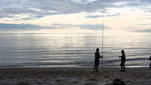 People standing on beach against sky during sunset