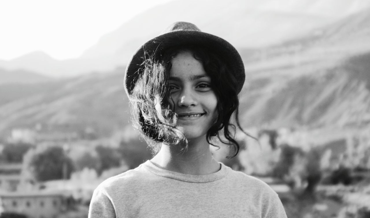 PORTRAIT OF SMILING WOMAN AGAINST MOUNTAINS