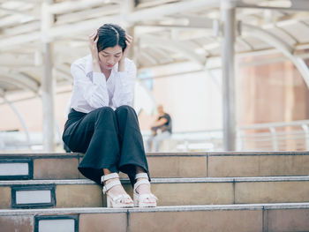 Low angle view of thoughtful young woman sitting outdoors