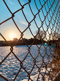 Close-up of chainlink fence against sky during sunset