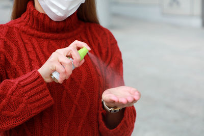 Woman wearing protective medical mask spraying alcohol sanitizer on her hands in modern city street