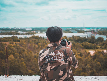 Rear view of man photographing against sky