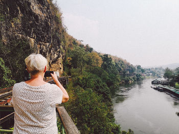 Rear view of person photographing through smart phone against sky