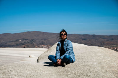 Portrait of smiling young woman sitting on land against blue sky