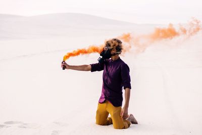 Man in gas mask holding distress flare on desert