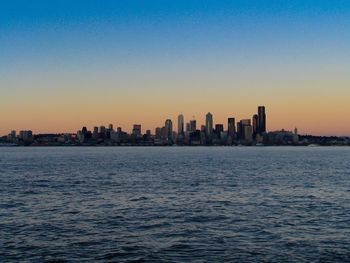 Sea by cityscape against clear sky during sunset