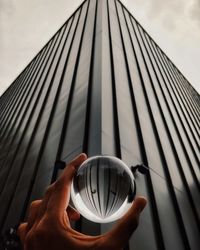 Cropped hand holding crystal ball against building