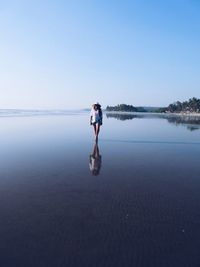 Full length of young woman walking at beach against clear sky