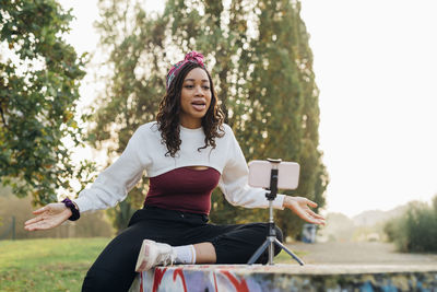 Young woman live streaming through mobile phone at park