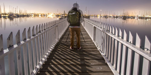 Rear view of woman standing on footbridge over lake