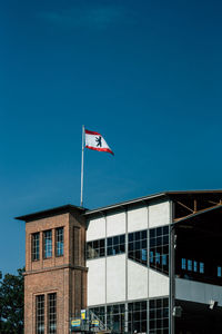 Low angle view of flag against buildings against clear blue sky