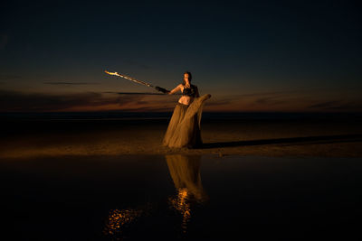 Woman standing at beach against sky during sunset