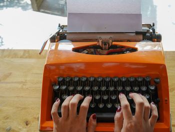 Cropped hands of woman typing on typewriter at table