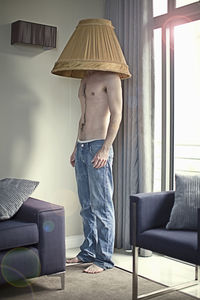 Shirtless man with lamp shade on head standing at home