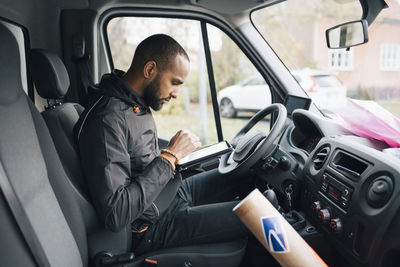 Side view of male worker using digital tablet while sitting in delivery van