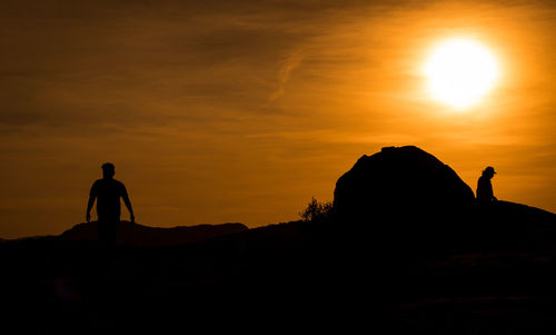 Silhouette man standing on rock against sky during sunset