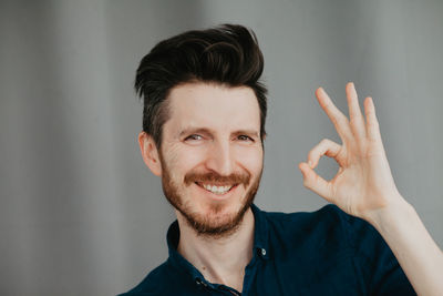 Handsome young man in a blue shirt by a grey background doing ok. smiling face. place for text. 